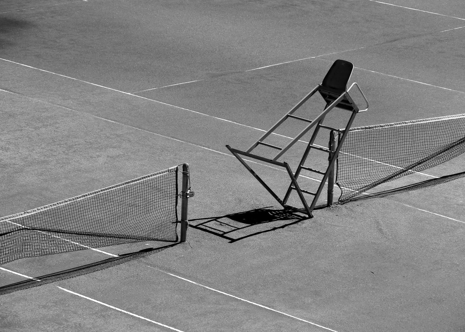 Lege tennisbaan met scheidsrechtersstoel en lange schaduwen