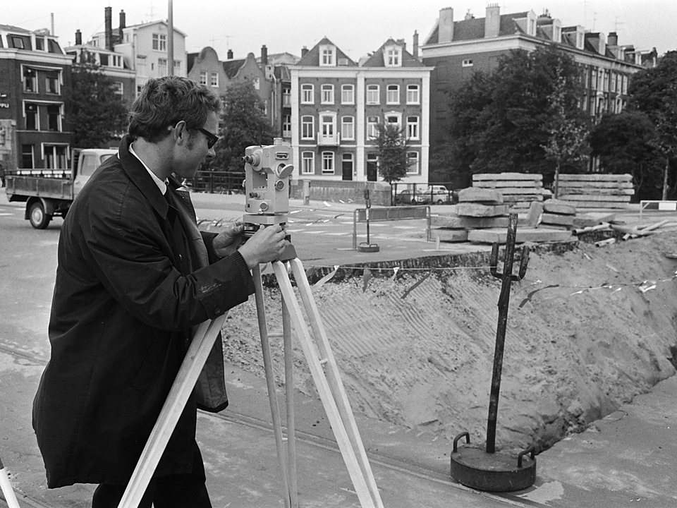 Landmeter met een waterpasinstrument langs een pas gegraven sleuf