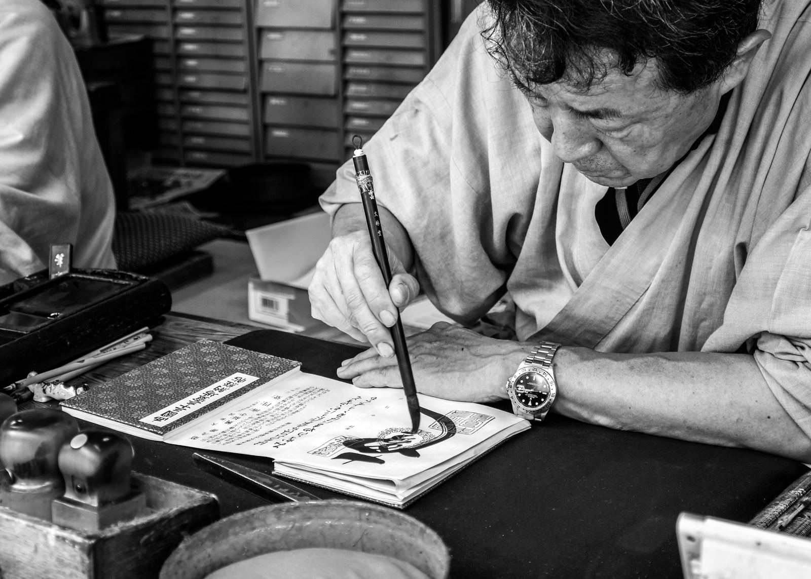 Man schrijft met de hand in een boek, letterkasten op de achtergrond